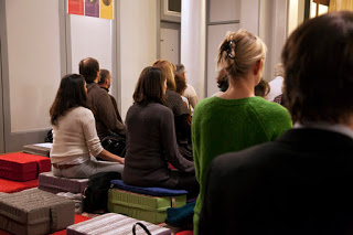 Photo d'ensemble de pratiquants vus de dos méditant sur coussin dans une salle
