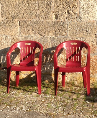Photo de deux chaises en plastique rouges posées devant un mur de pierres taillées