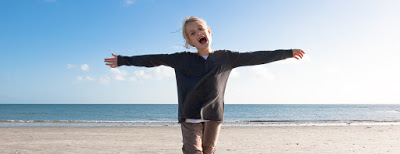 Photo de face d'un enfant sur une plage, debout, les bras écartés à l'horizontal