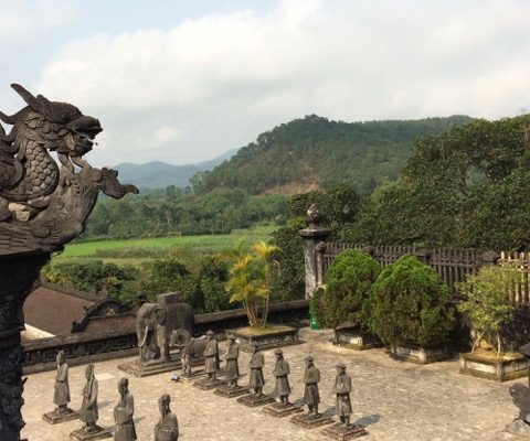 Photo en plongée d'une cour en pierre où sont alignées deux rangées de statues, avec à gauche au premier plan la sculpture d'un dragon