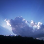 Photo d'un grand nuage, dans un ciel à diverses nuances de bleu, des bords duquel jaillissent des rayons de lumière