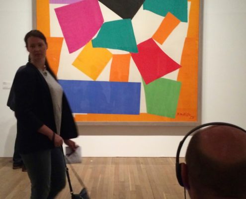 Photo du tableau "L'escargot" de Matisse, avec au premier plan, à droite, un homme assis avec des écouteurs et à gauche, une femme, la tête tournée vers l'objectif