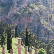 Superbe photo avec au premier plan les colonnes et vestiges en pierres d'un ancien édifice, dans un cadre naturel de collines boisées et de roches rouges