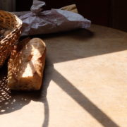 Photographie d'une table au soleil, sur laquelle sont posés un morceau de baguette et un panier rempli de noix avec un casse-noix.