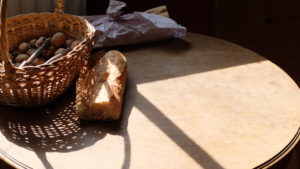 Photographie d'une table au soleil, sur laquelle sont posés un morceau de baguette et un panier rempli de noix avec un casse-noix.