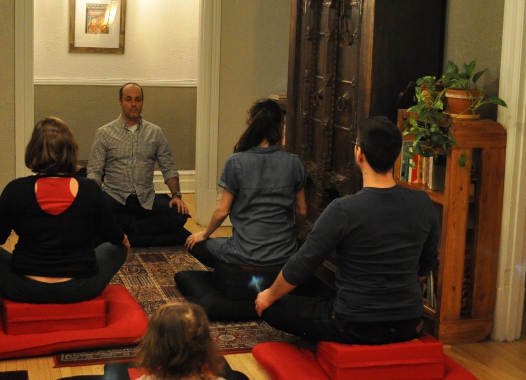 Photo de la salle de pratique de l'École occidentale de méditation, fondée par Fabrice Midal, à Montréal, avec, assis de face, Philippe Blackburn et quelques pratiquants de dos.