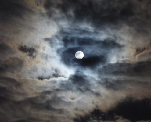 Photographie d'un ciel nuageux, une nuit de pleine Lune.