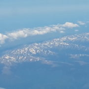 Photographie d'une chaine de montagnes surmontée d'une trâinée de nuages vus du ciel.