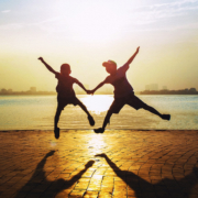 Photographie montrant deux enfants sautant devant un coucher de soleil. Leurs bras et leurs jambes s'unissent en forme de cœur.