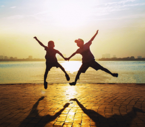 Photographie montrant deux enfants sautant devant un coucher de soleil. Leurs bras et leurs jambes s'unissent en forme de cœur.
