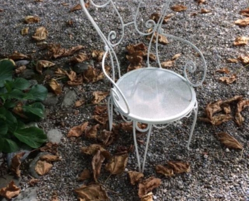 Photographie d'une chaise de jardin sur un sol gravillonné parsemé de feuilles mortes