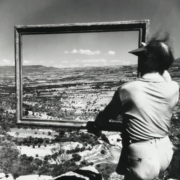 Photographie par Willy Ronis du peintre André Lhote vue de dos portant un cadre vide devant un paysage à Gordes.