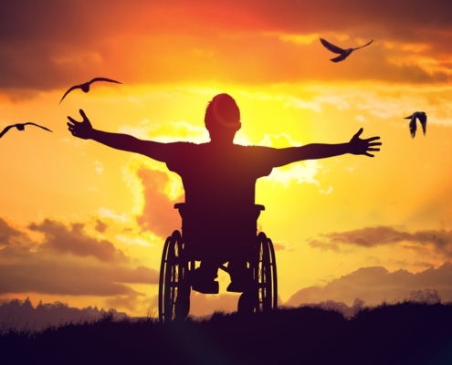 Photo d'un homme en chaise roulante ouvrant grand les bras face au soleil orangé