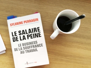 Photo du livre de Sylvaine Perragin, "Le salaire de la peine", posé sur une table à côté d'une tasse de café