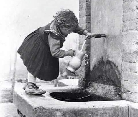 Enfant remplissant un pichet à eau à une fontaine, noir et blanc