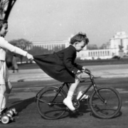 Photo noir et blanc de Robert Doiseau : un enfant en rolleur est tiré par un enfant à vélo en s'accrochant à sa jupe